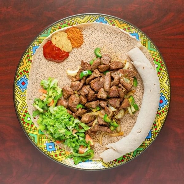 Elsi Ethiopian Restaurant's Tibs, a meat dish with injera, salad, and spices on a colorful plate.