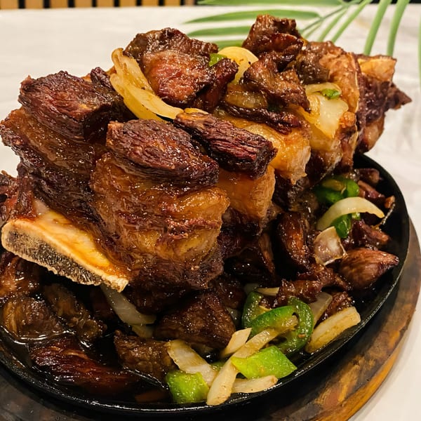 Sizzling Ethiopian beef short ribs with onions and green peppers on a black skillet.