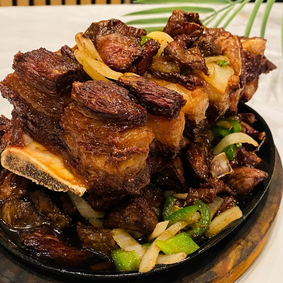 Sizzling Ethiopian beef short ribs with onions and green peppers on a black skillet.